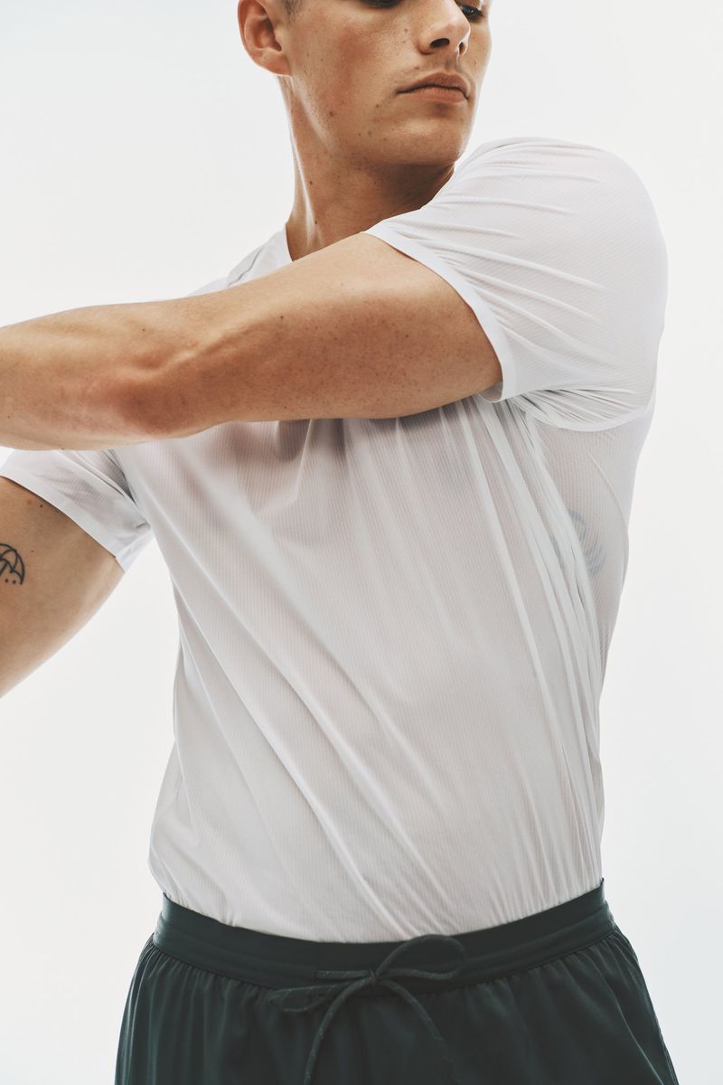 Model Finley Prentice stretching his arm wearing a white athletic t-shirt and dark drawstring shorts against a white backdrop.