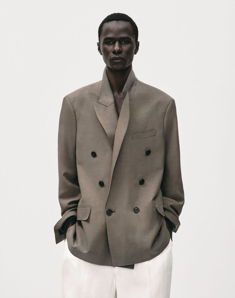 Model Malick Bodian wearing an oversized taupe double-breasted blazer and white trousers against a plain white studio backdrop.