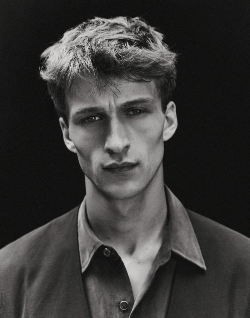 Black and white studio portrait of model Vasko Luyckx wearing a collared shirt and tailored jacket against a black backdrop.
