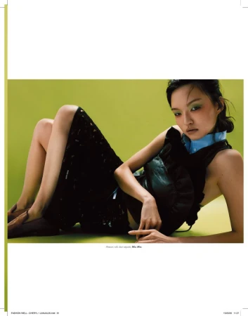Model reclining on a vibrant green studio backdrop wearing a black ruffled top, dark midi skirt, and brown loafers for Elle Indonesia.