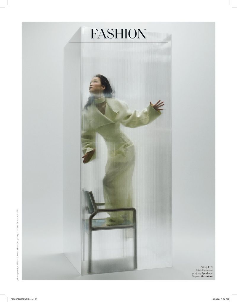Model Shinyu Pan stands on a chair enclosed within a fluted translucent acrylic box wearing a pale tailored suit in a studio.