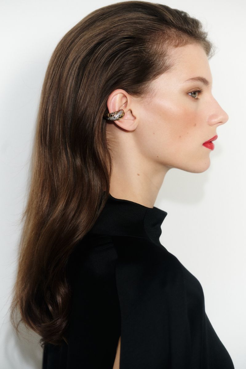 Model Paula Engbert in profile wearing an embellished ear cuff and black high-neck top against a white studio background.