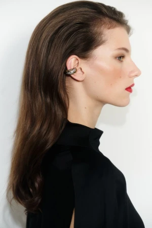 Model Paula Engbert in profile wearing an embellished ear cuff and black high-neck top against a white studio background.