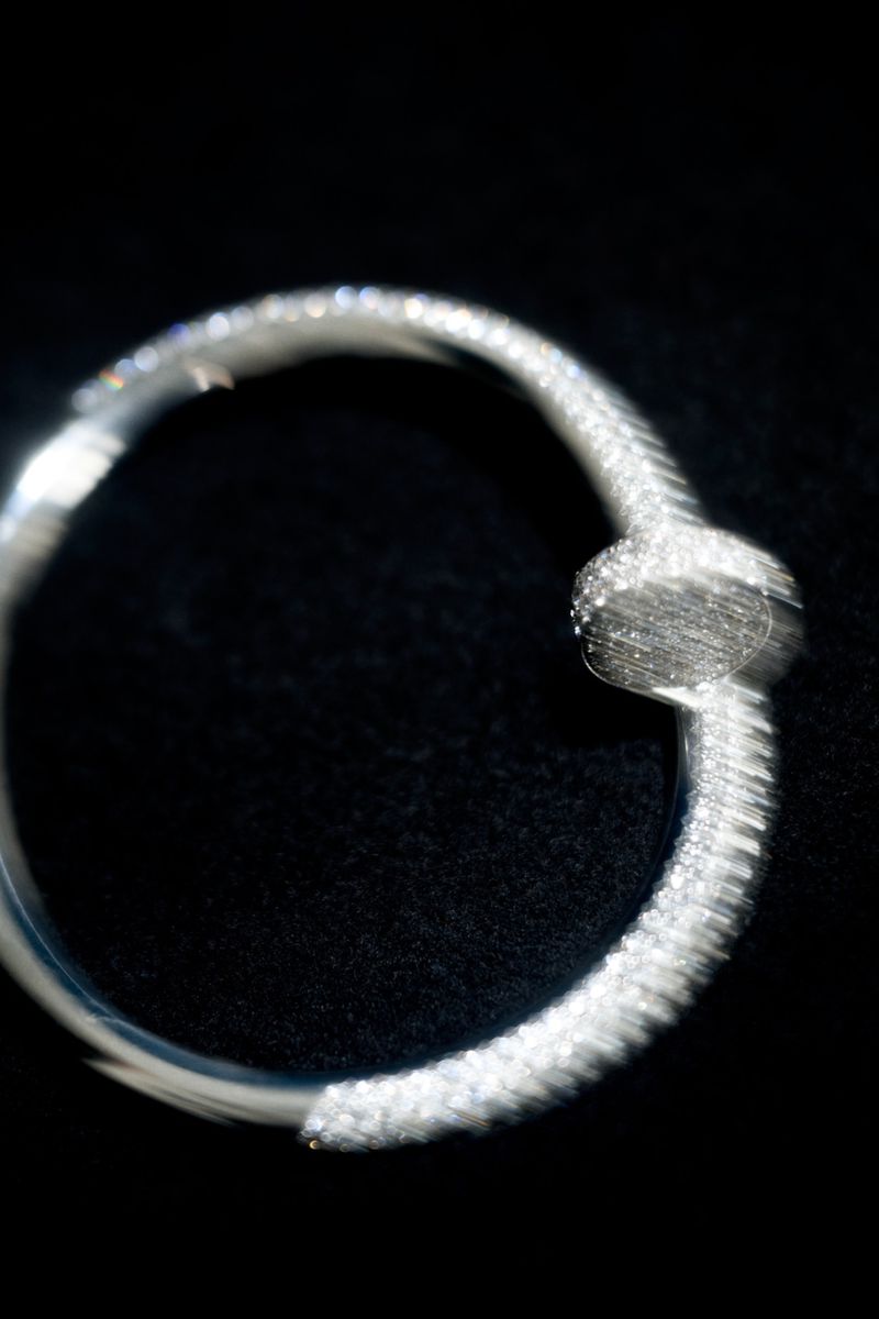 Macro photograph of a diamond-paved nail-shaped ring with a motion blur effect against a dark black background.