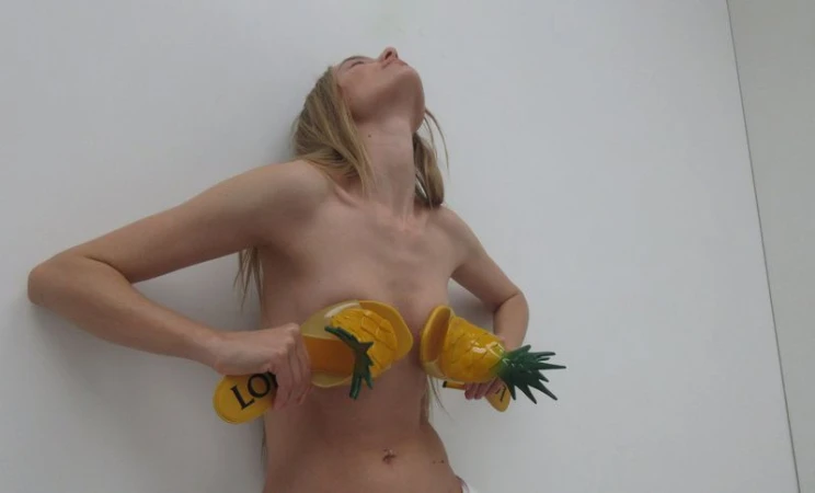 Model holding yellow pineapple-detailed sandals against her chest in a white studio environment.