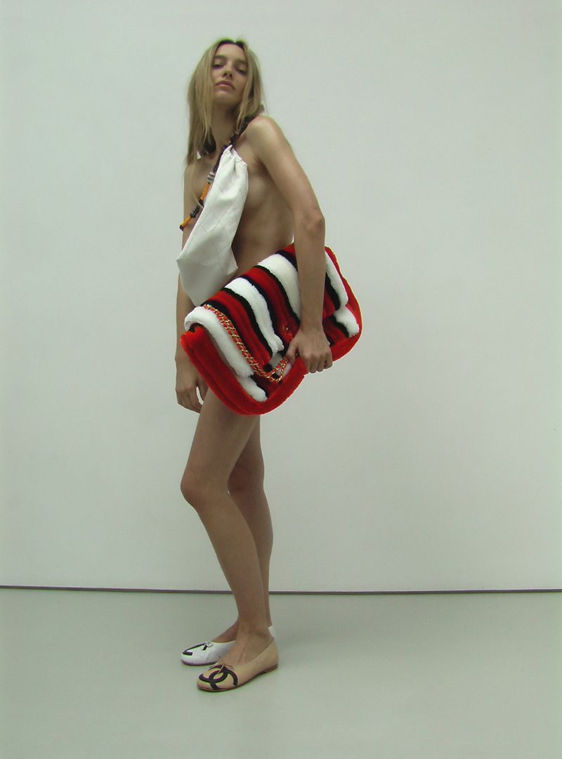 Model Maya Stepper posing with an oversized red, black, and white striped fluffy bag against a white studio wall.