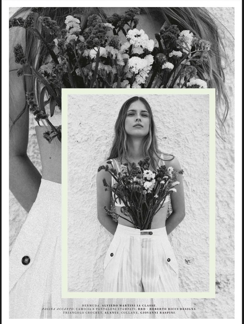 Monochrome fashion shot of a young adult woman with long hair, holding a large bouquet of white flowers against a textured wall.
