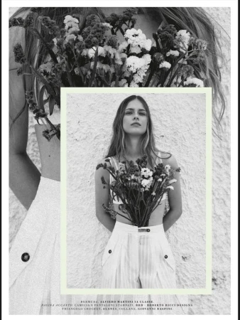 Monochrome fashion shot of a young adult woman with long hair, holding a large bouquet of white flowers against a textured wall.