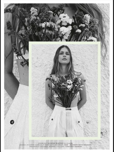 Black and white fashion editorial image featuring a female model holding a large bouquet of wildflowers against a textured wall.