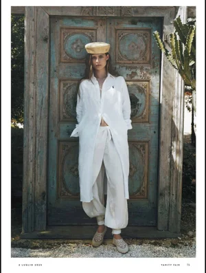 Model Zoe Petit in white linen outfit and yellow beret posing in front of an ornate weathered wooden door for Vanity Fair Italia Estate