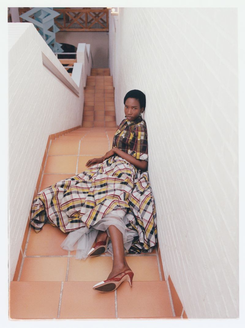Model Zayna Cisse seated on a terracotta tiled staircase wearing a plaid dress and pointed heels.
