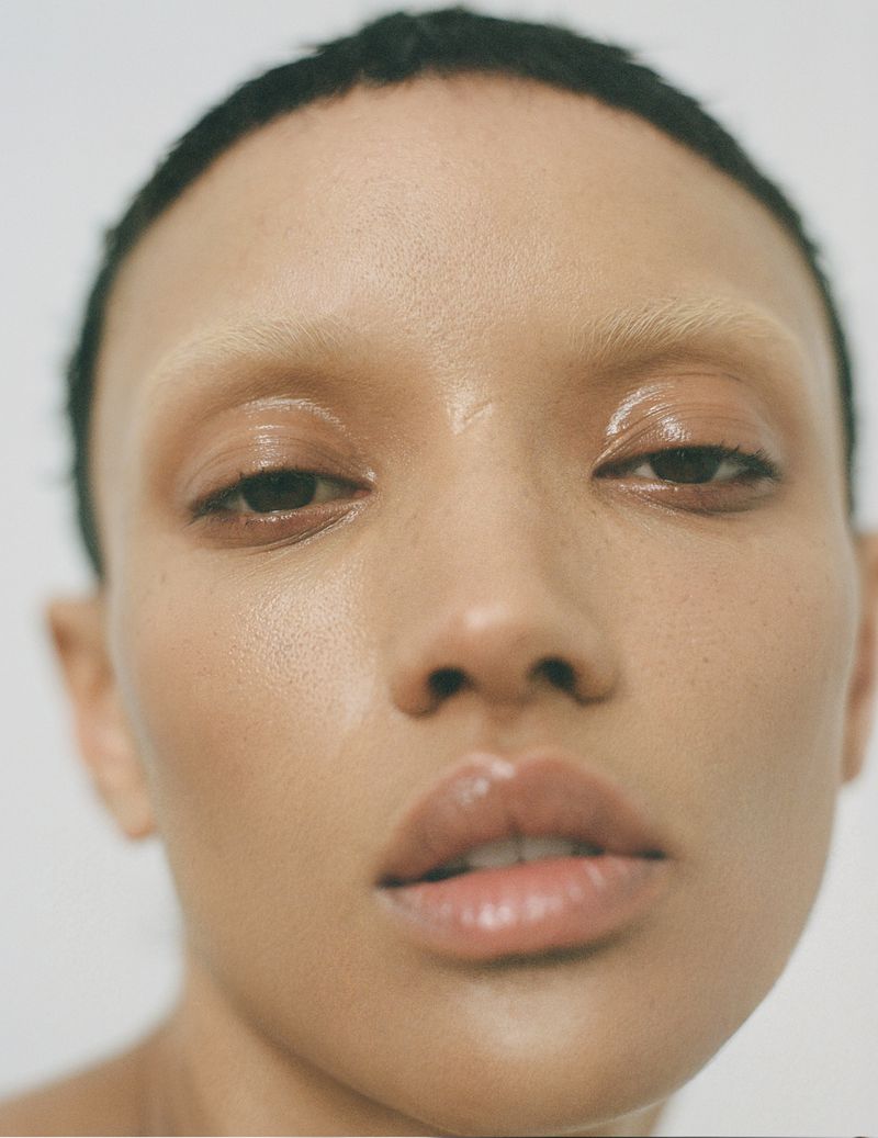 Close-up beauty portrait of Georgia Palmer with bleached eyebrows and glossy skin against a white studio background.