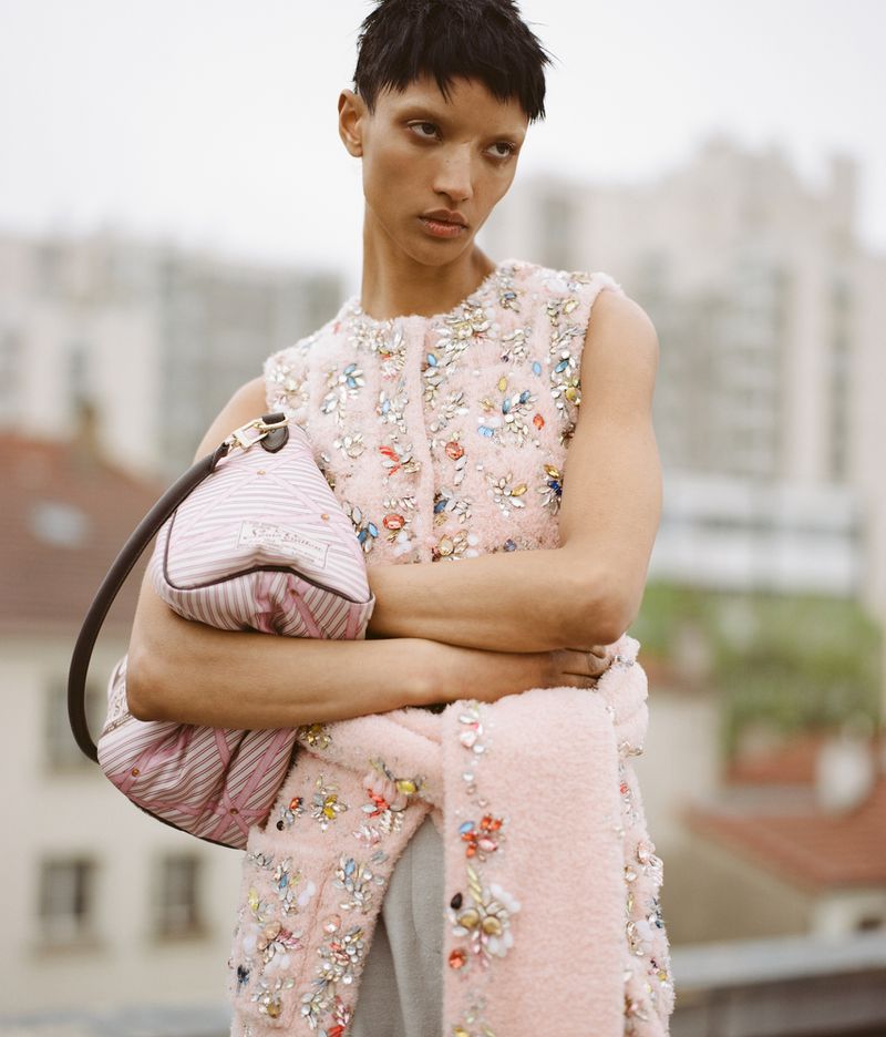Model Georgia Palmer wearing an embellished light pink top and holding a striped pink bag outdoors.