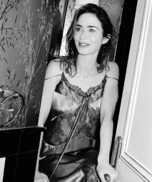 Black and white portrait of Emily Blunt wearing a lace-trimmed satin slip dress standing in a doorway.