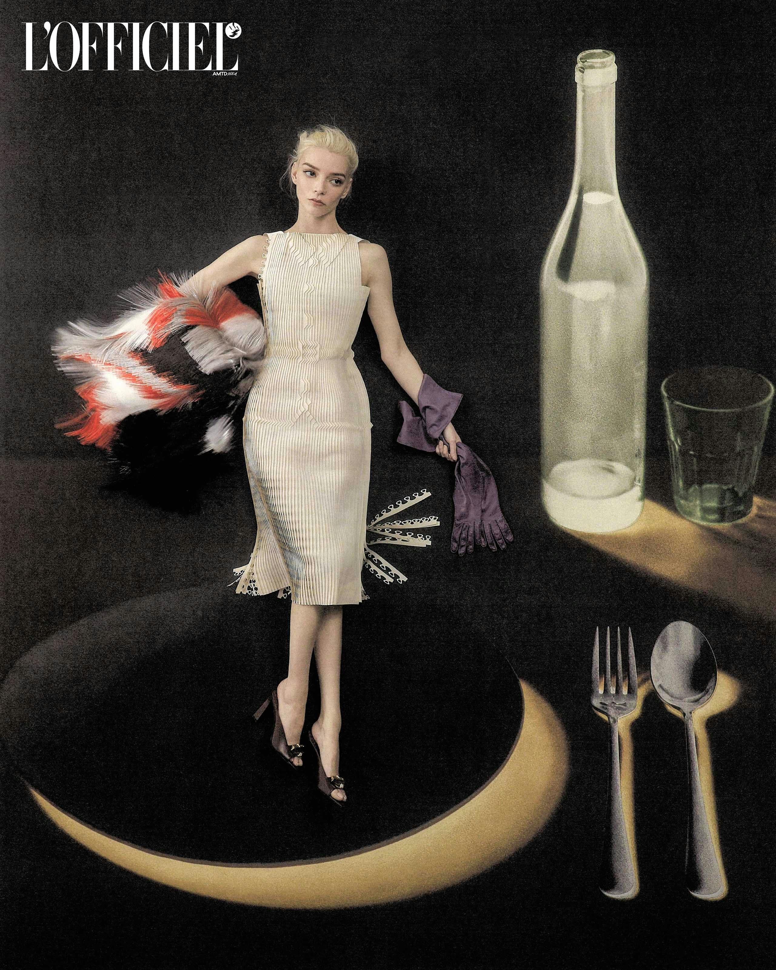 Anya Taylor-Joy in a textured cream dress standing beside large props including a glass bottle and cutlery on a dark background.