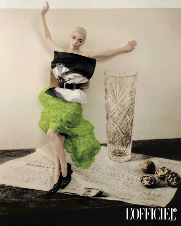 Anya Taylor-Joy in a lime green textured skirt and folded bodice posing beside a crystal vase and walnuts on newspaper.