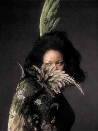 Editorial portrait of Rihanna in a feathered headpiece and embroidered winged cape against a dark textured backdrop.