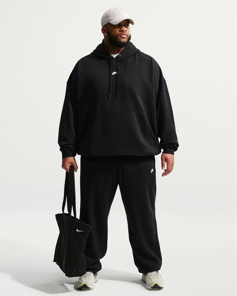 Model Steven Green wearing a black Nike oversized hoodie, matching sweatpants, and a beige cap against a white background.