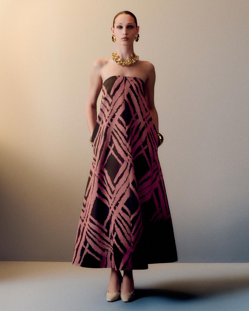 Elegant adult female wearing a black and pink strapless dress with jewelry, in a full shot against a neutral studio backdrop.