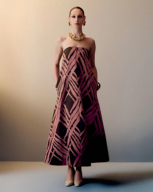 Elegant adult female wearing a black and pink strapless dress with jewelry, in a full shot against a neutral studio backdrop.