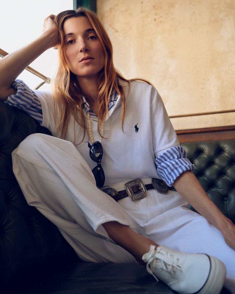 Woman wearing a white Polo Ralph Lauren shirt, concho belt, and white pants seated on a tufted leather sofa.