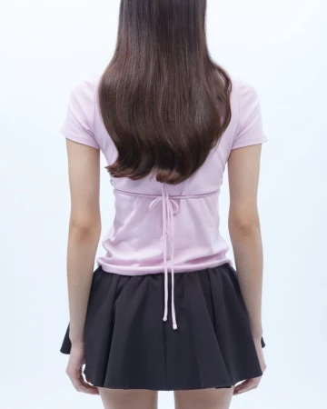 Back view of a woman wearing a lilac t-shirt tied at the waist and a black mini skirt against a clean white backdrop in studio lighting.