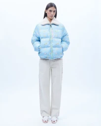 A model standing in a light blue gingham puffer jacket with a fleece collar and cream trousers against a plain white background.