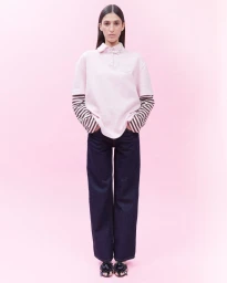 Model standing centered wearing a layered pink polo shirt and dark denim jeans against a pale pink background.