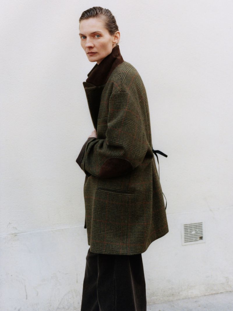 Model Karolin Wolter wearing an oversized olive plaid coat with elbow patches against an off-white wall for ssstein.
