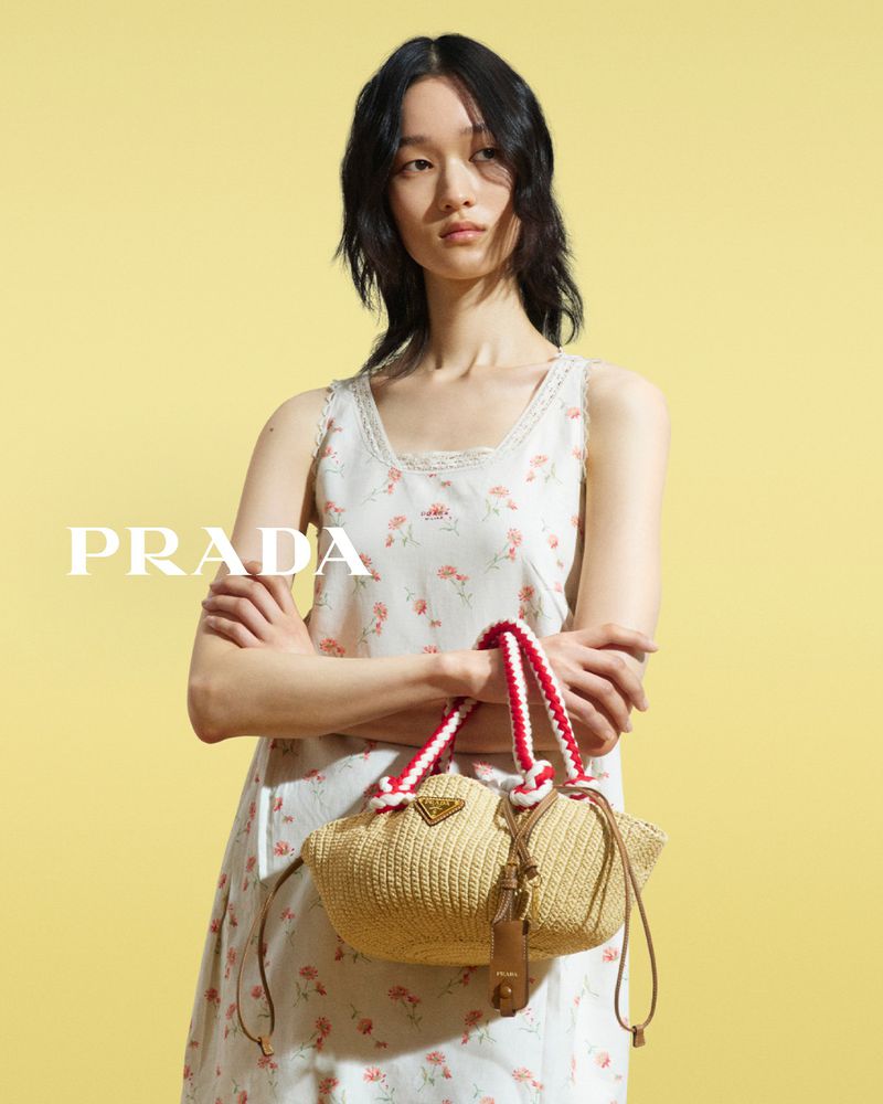 Woman with Prada handbag stands against a yellow backdrop, modelling fashion, in a medium studio shot with soft lighting.