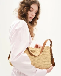 A woman holding a woven straw shoulder bag with brown leather straps against a solid white studio background.