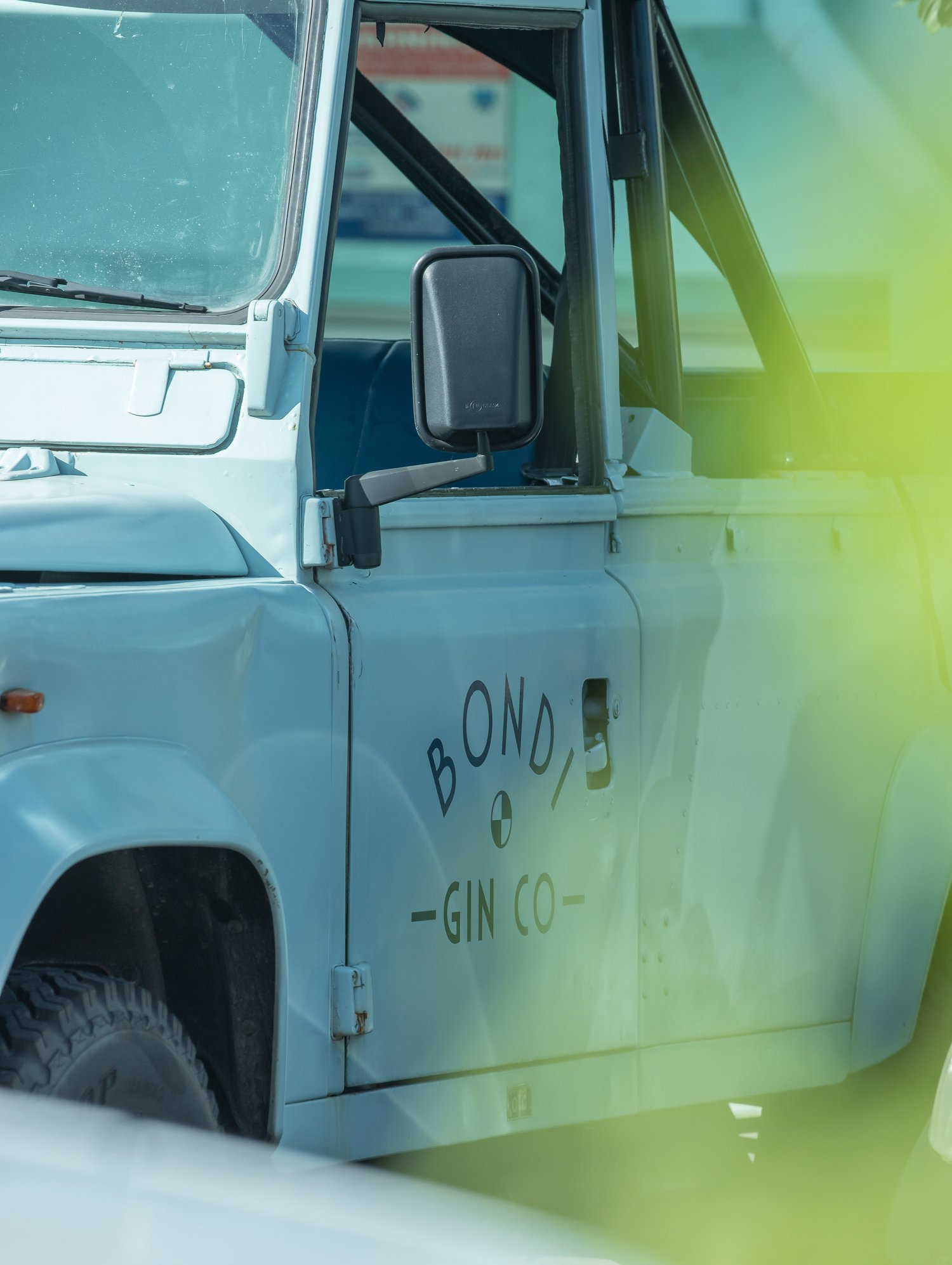 Light blue off-road vehicle with gin branding is partly obscured by foliage in this outdoor shot. Vehicle has tire visible.