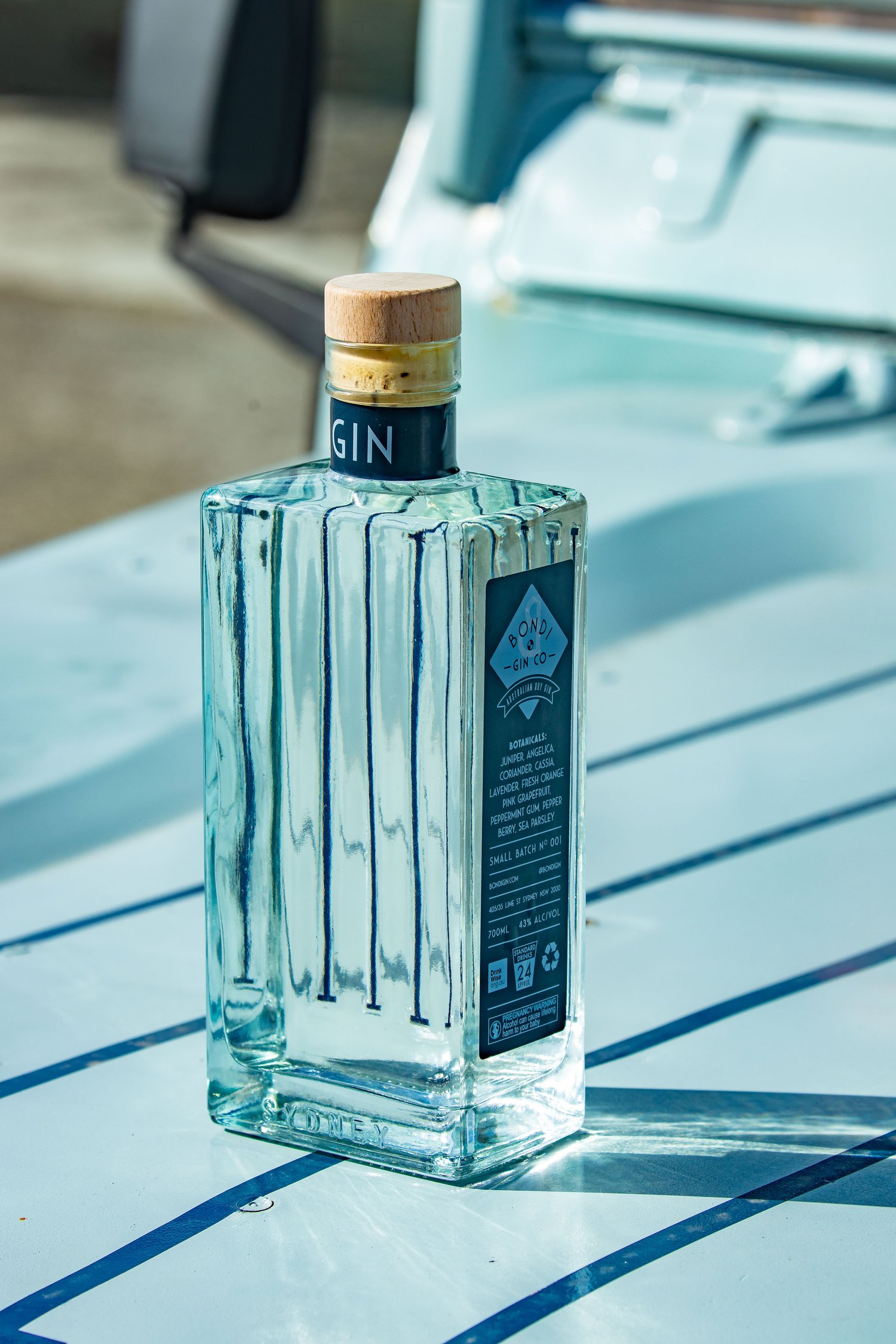 Elegant glass bottle of gin with wooden cap, sitting on a blue-and-white surface, showcasing clear liquor and textured design.
