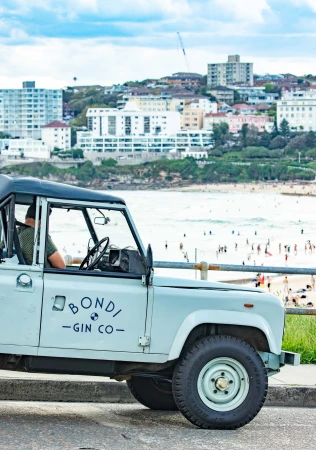 Light blue gin company SUV parked near Bondi Beach, Sydney, Australia, showcasing the coastline and cityscape during daylight.