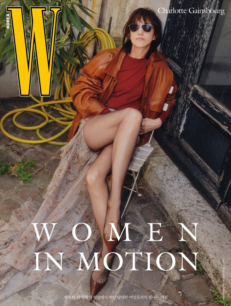 Charlotte Gainsbourg poses on a chair in a leather jacket and patterned skirt for W Korea magazine cover in an outdoor setting.