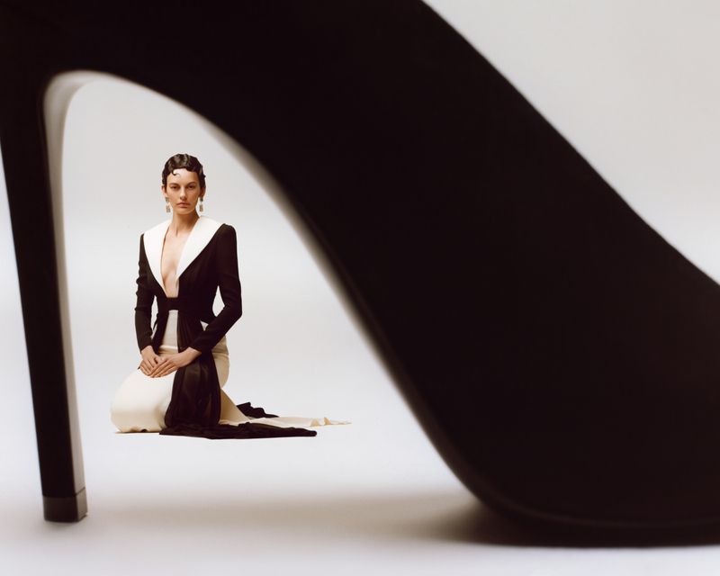 Model Amanda Murphy kneels in a black and white gown framed beneath the arch of a large black stiletto heel against a white backdrop.