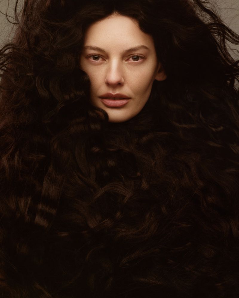 Close-up portrait of model Amanda Murphy enveloped in voluminous dark textured curls against a muted backdrop.