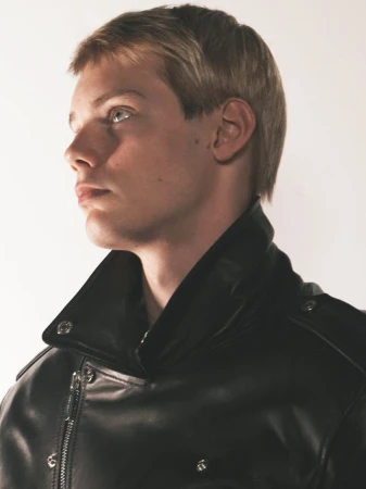 Close-up portrait of a male model in a black leather jacket against a light background, photographed by David Sims.