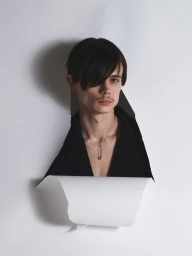 Model Finn Collins looking through a torn white paper backdrop wearing an open black blazer and necklace.