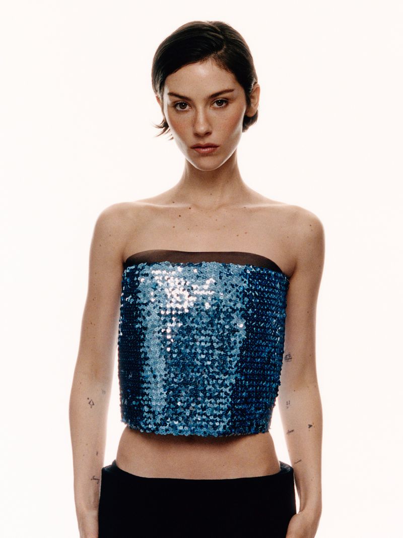 Gracie Abrams wearing a strapless blue sequined crop top and black bottoms against a pure white studio background.