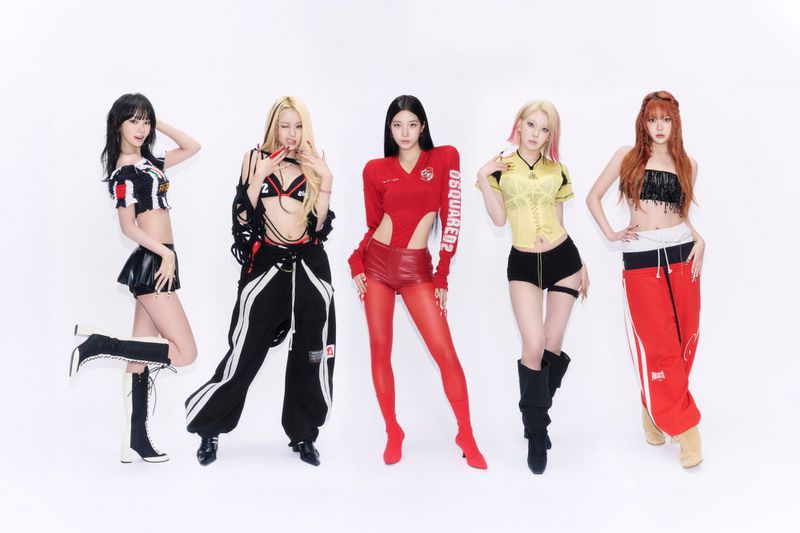 Five members of K-pop group LE SSERAFIM posing against a white studio background in sporty red, black, and yellow streetwear.