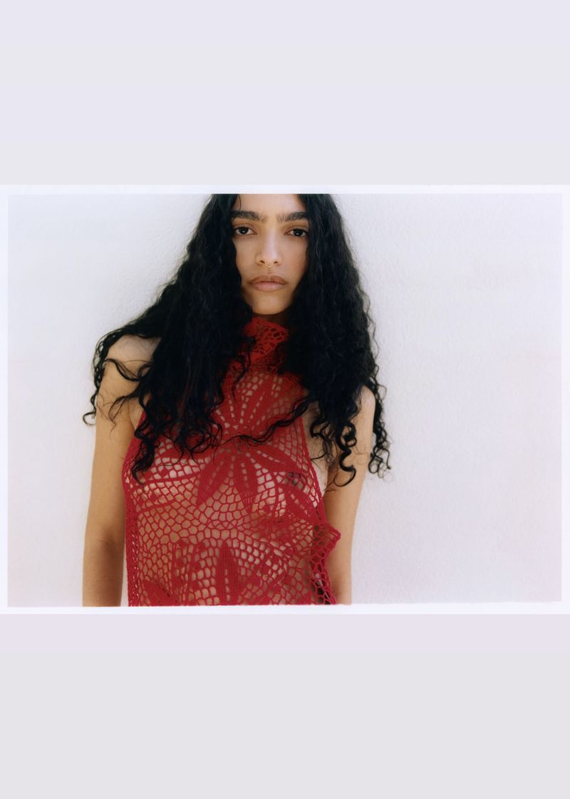 Model Anita Pozzo wearing a sheer red floral crochet top against a white background.