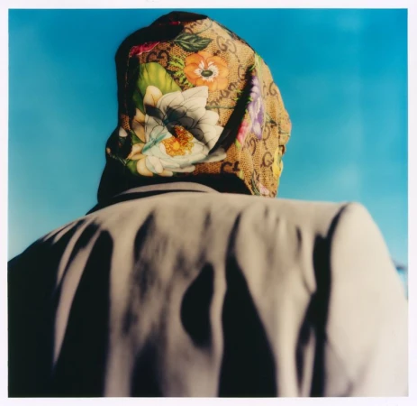 Rear view of a person wearing a floral monogram headscarf and beige blazer against a clear blue sky.