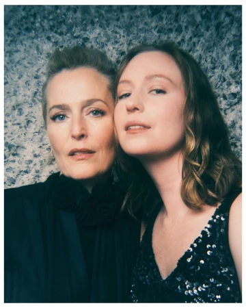 Gillian Anderson and Hannah Einbinder posing closely in black attire against a textured grey stone wall.