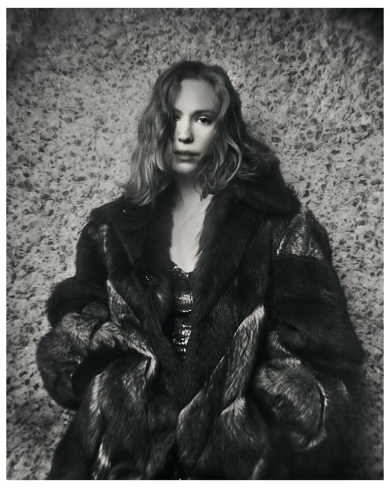 Black and white portrait of Hannah Einbinder wearing an oversized fur coat against a textured stone wall.