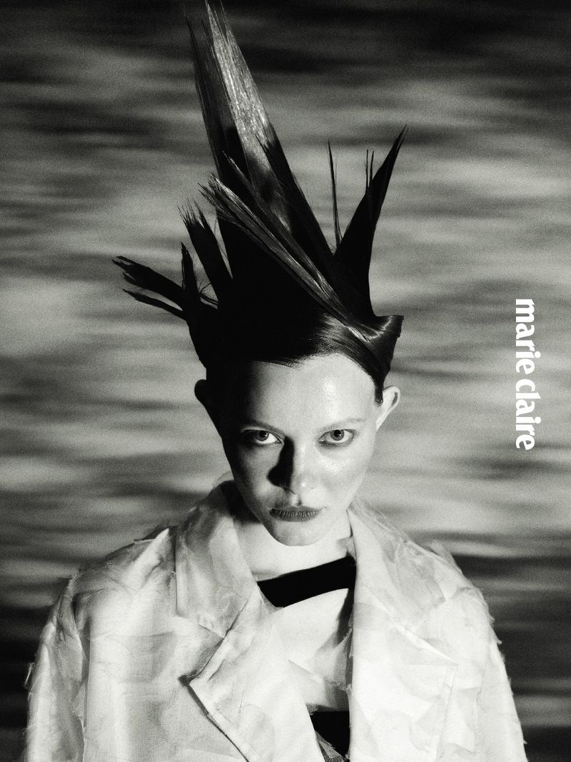 Monochrome fashion portrait of a woman with a dramatic spiky sculptural hairstyle wearing a textured light coat.