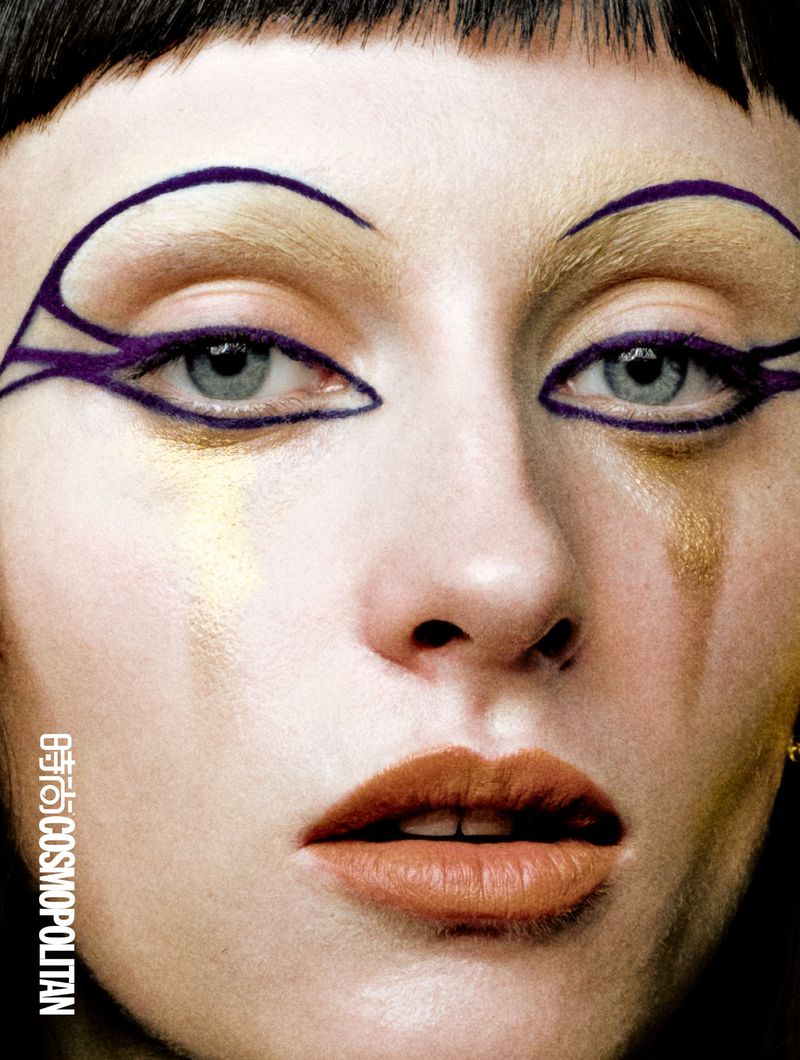 Close-up beauty portrait of model Hannah Vincent with graphic purple eyeliner, gold accents, and terracotta lipstick.