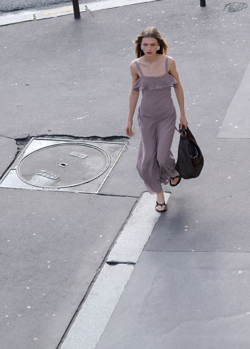 Model Ella McCutcheon walks on a paved street wearing a dusty mauve strapped jumpsuit and holding a black leather tote bag.