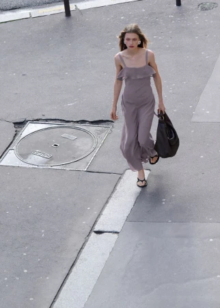 Model Ella McCutcheon walks on a paved street wearing a dusty mauve strapped jumpsuit and holding a black leather tote bag.