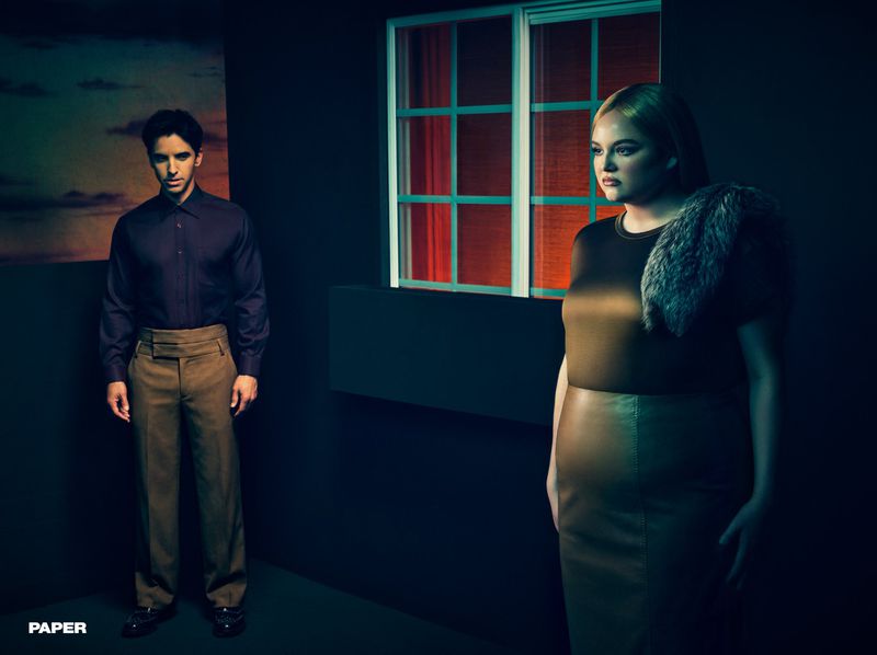Megan Stalter and a man standing in a moody, dimly lit studio room beside a window with red light for Paper Magazine.